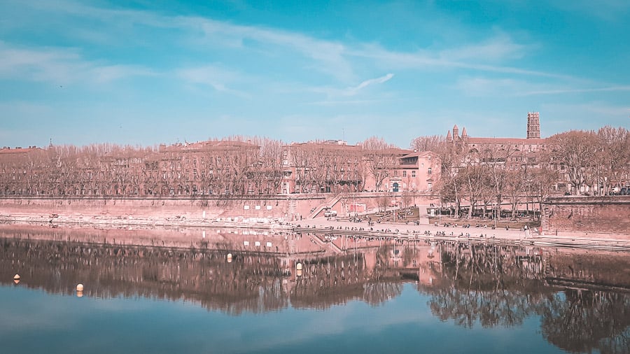 Couples sitting along the waterside with buildings in background, Toulouse