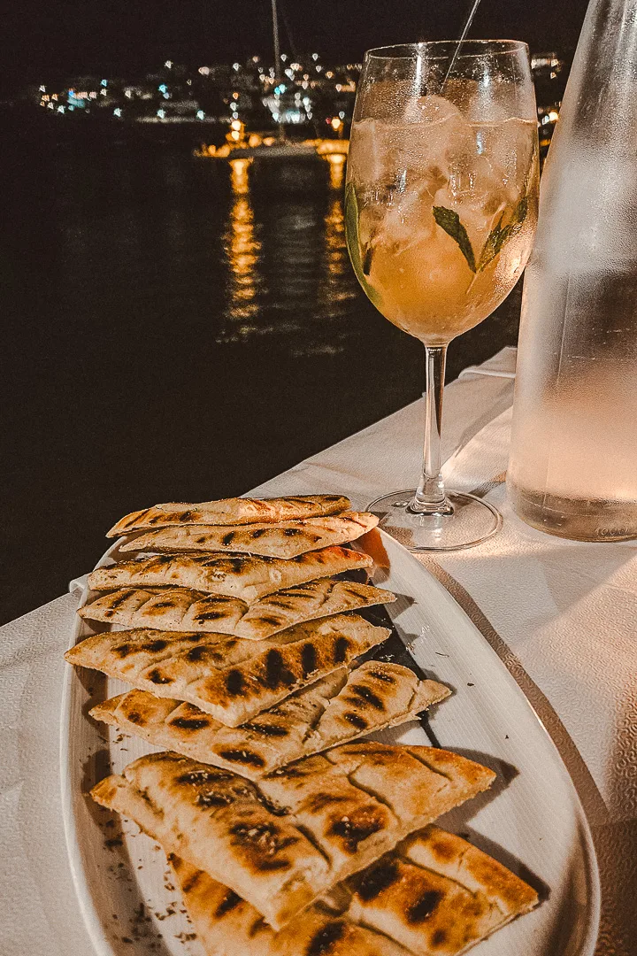 plate of pita bread with wine glass on table in front of sea, Batsi