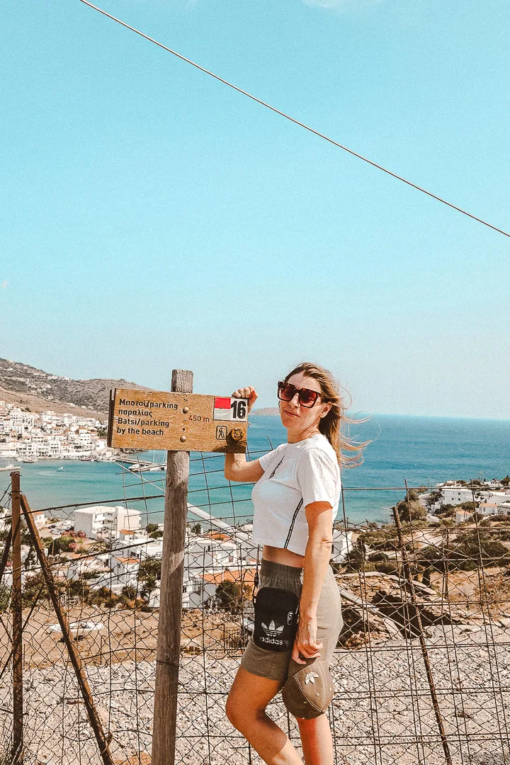 woman in front of hiking waymarking signs, Batsi village, Andros