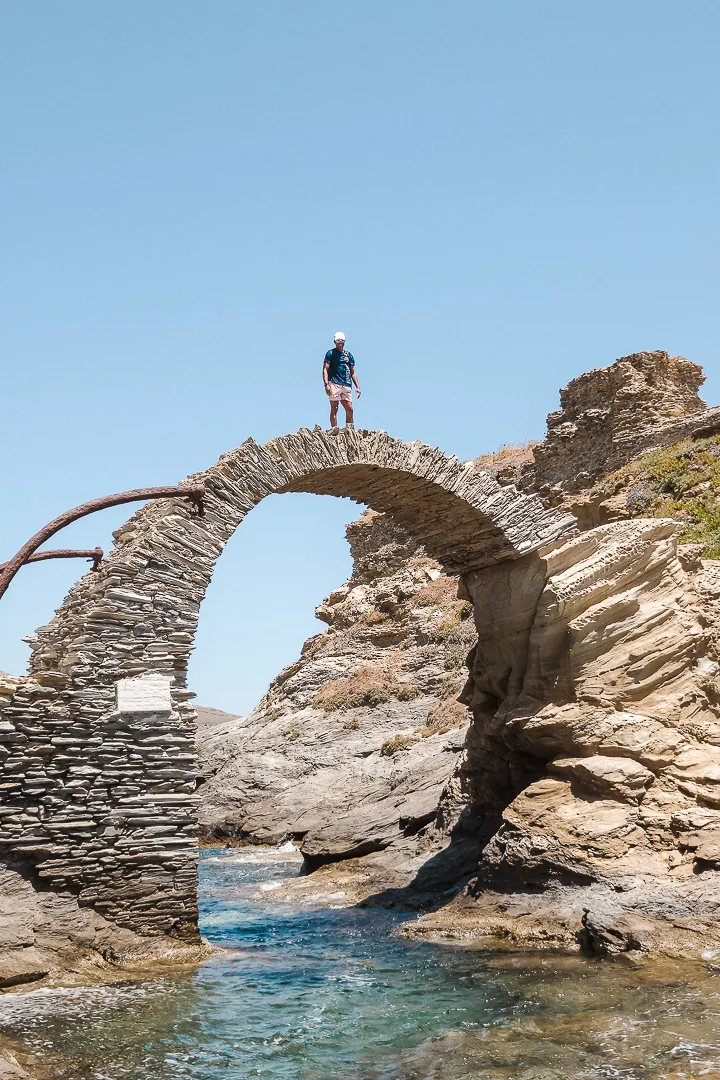 man stood on stone bridge from chora town, Andros, to the castle ruins
