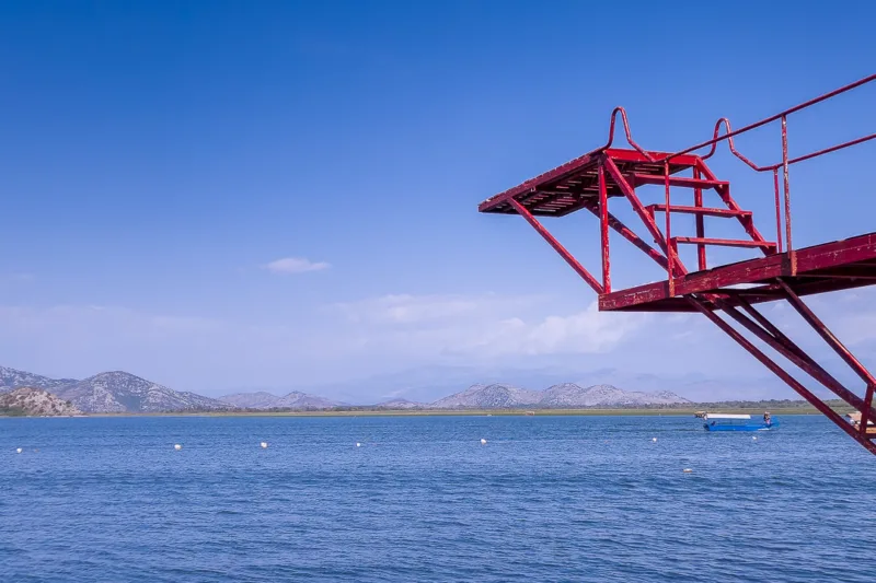 diving board over Lake Skadar, boat on water, mountains in background